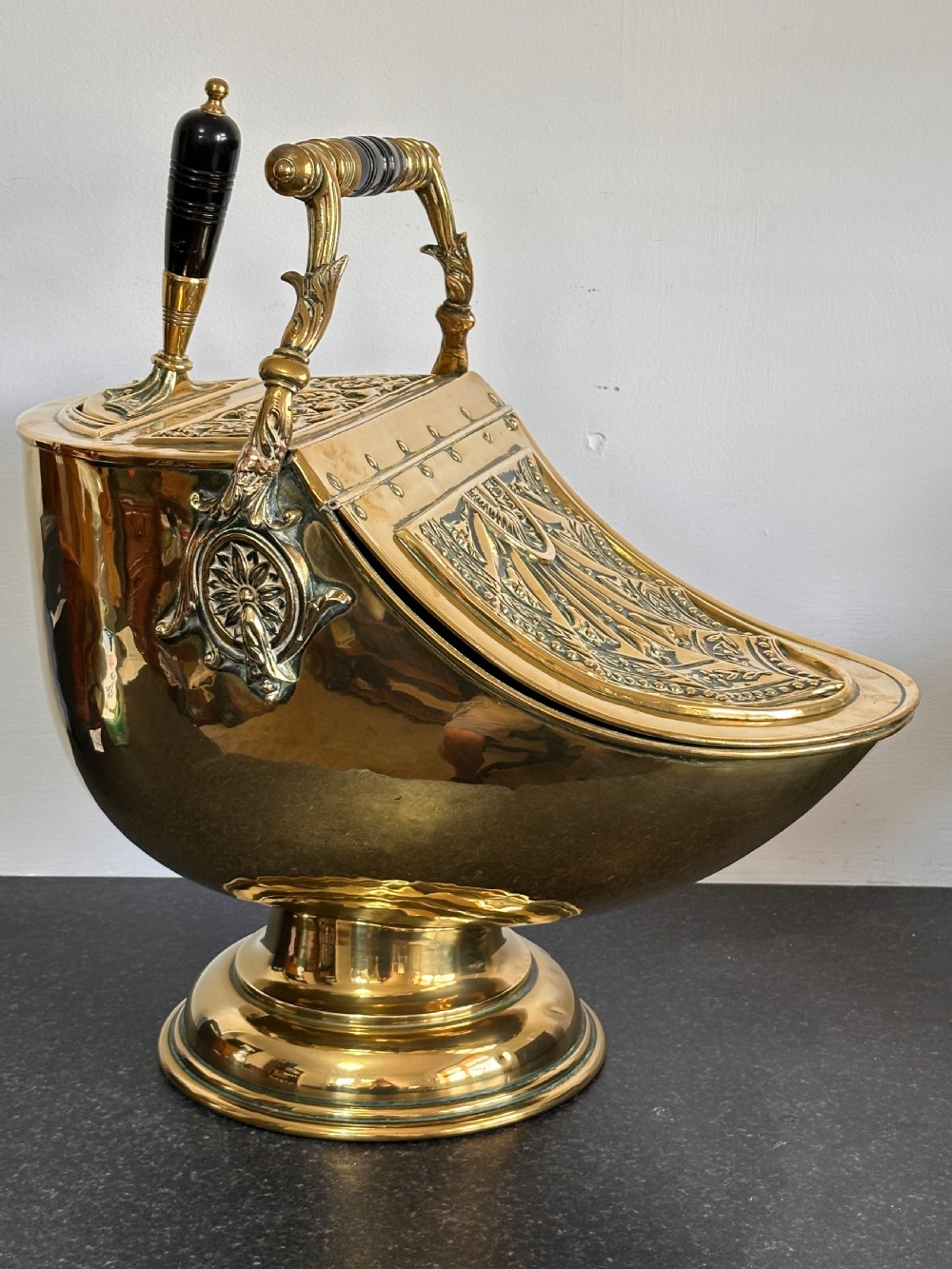 Victorian brass coal scuttle featuring elaborate repousse relief patterns, a pedestal base, and an ebonised wooden handle. View II