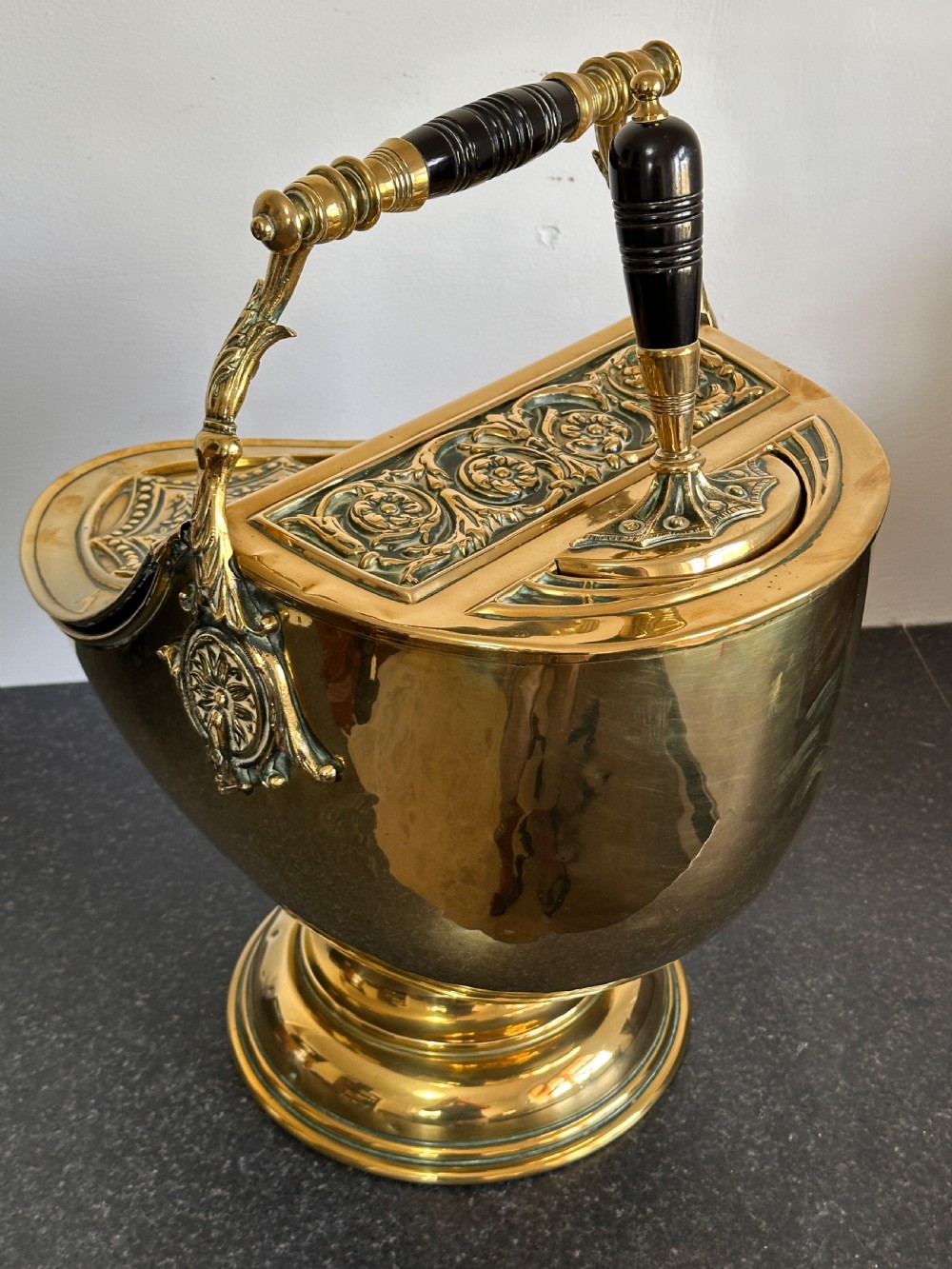 Victorian brass coal scuttle featuring elaborate repousse relief patterns, a pedestal base, and an ebonised wooden handle. View III