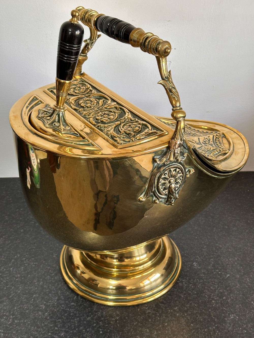 Victorian brass coal scuttle featuring elaborate repousse relief patterns, a pedestal base, and an ebonised wooden handle. View IV