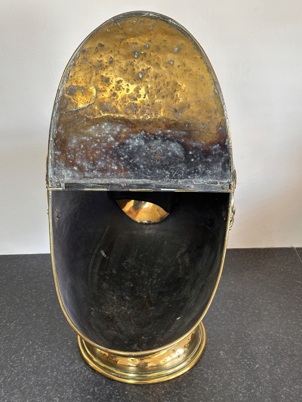 Victorian brass coal scuttle featuring elaborate repousse relief patterns, a pedestal base, and an ebonised wooden handle. View VI