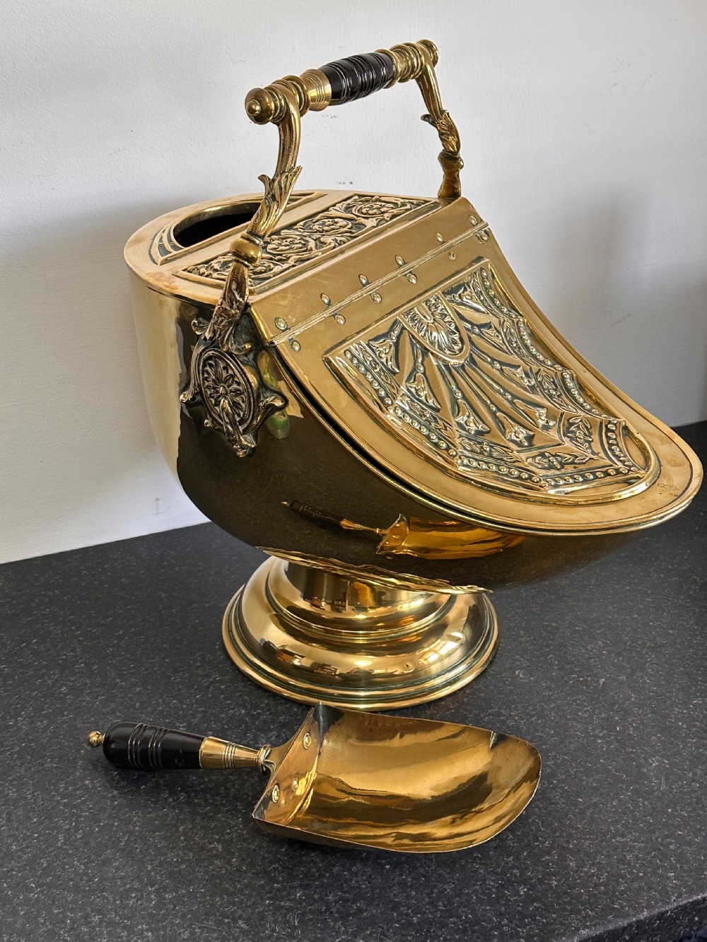 Victorian brass coal scuttle featuring elaborate repousse relief patterns, a pedestal base, and an ebonised wooden handle. View VII