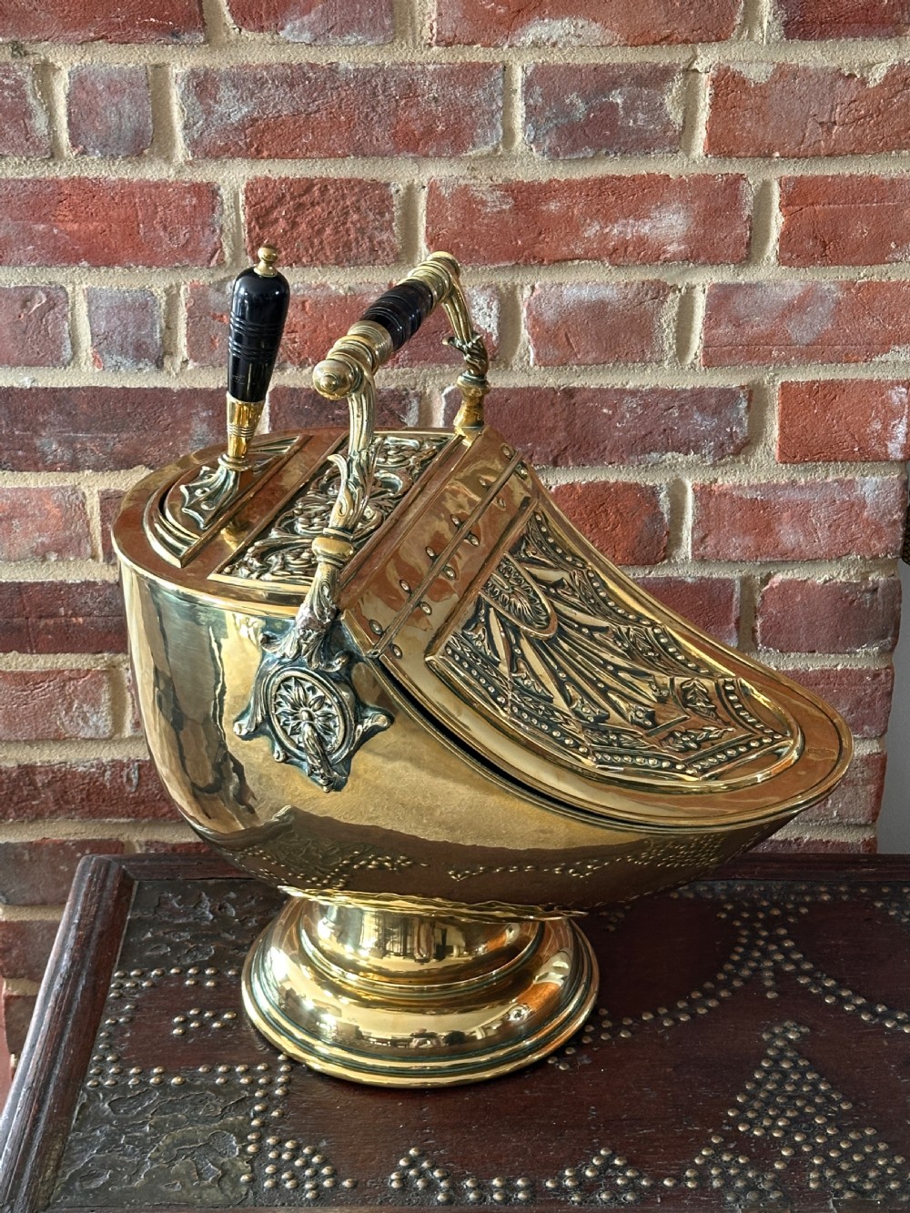Victorian brass coal scuttle featuring elaborate repousse relief patterns, a pedestal base, and an ebonised wooden handle. View IX