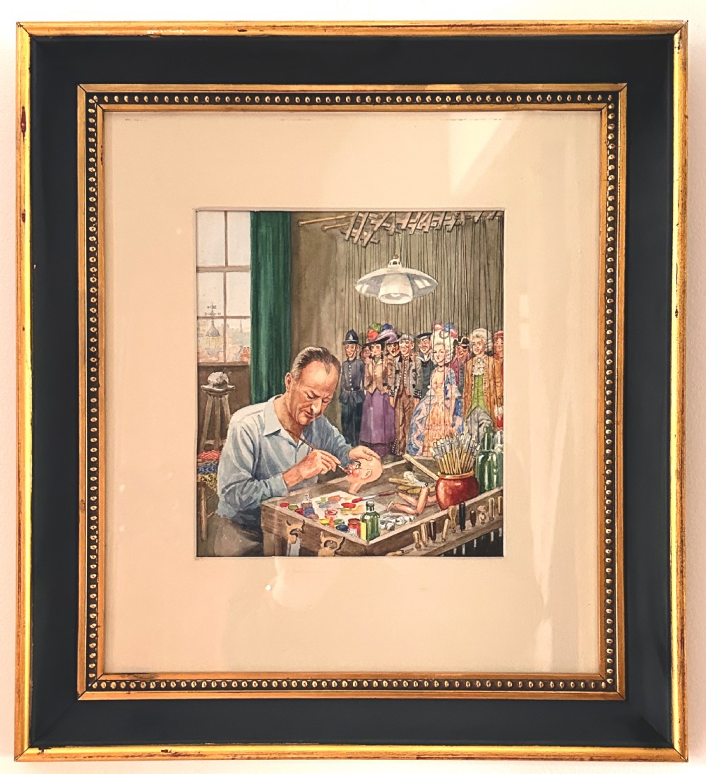A framed watercolour painting depicting a craftsman at a workbench painting a marionette head, surrounded by finished puppets hanging in the background.
