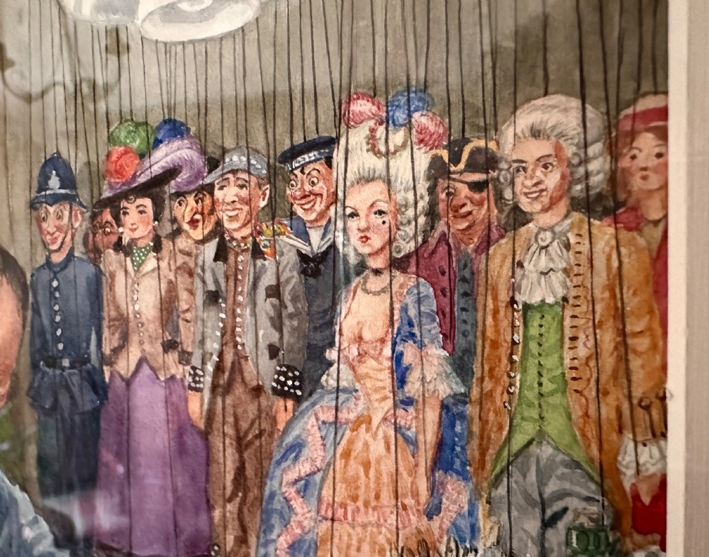 A framed watercolour painting depicting a craftsman at a workbench painting a marionette head, surrounded by finished puppets hanging in the background. View IV