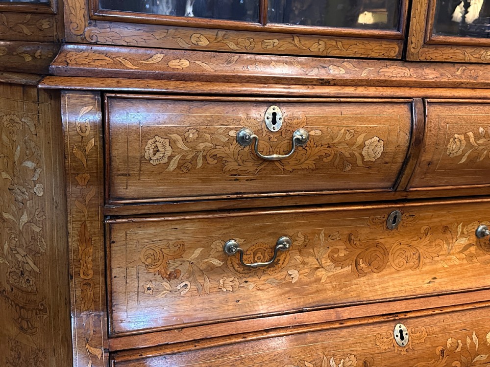 An 18th-century Dutch walnut display cabinet featuring a shaped bonnet top, glazed doors, intricate floral marquetry, and a lower bombe chest with drawers. View IV