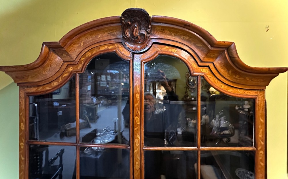 An 18th-century Dutch walnut display cabinet featuring a shaped bonnet top, glazed doors, intricate floral marquetry, and a lower bombe chest with drawers. View VII