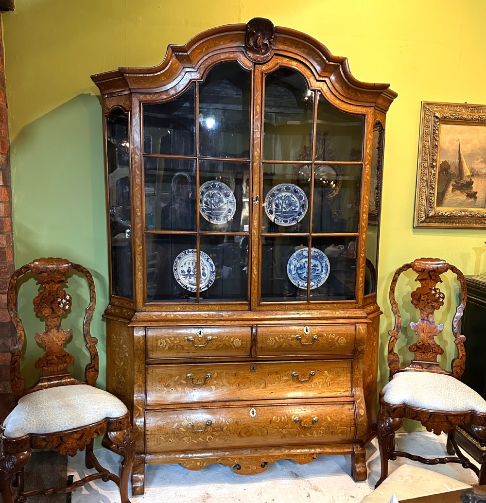 An 18th-century Dutch walnut display cabinet featuring a shaped bonnet top, glazed doors, intricate floral marquetry, and a lower bombe chest with drawers.