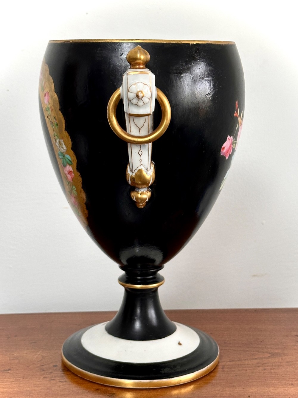 A black French porcelain goblet vase featuring gilt handles, a flared pedestal base, and a central painted medallion depicting a classical figure labelled Le Soir. View II