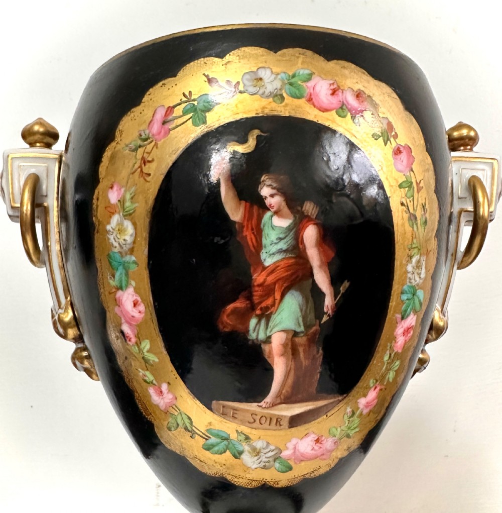 A black French porcelain goblet vase featuring gilt handles, a flared pedestal base, and a central painted medallion depicting a classical figure labelled Le Soir. View VI
