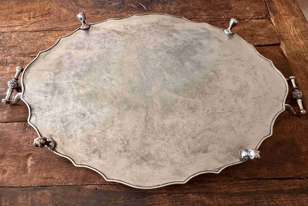 A large oval silver-plated tray featuring a scalloped gallery border, twin side handles, etched foliate surface decoration, and cast feet. View VII