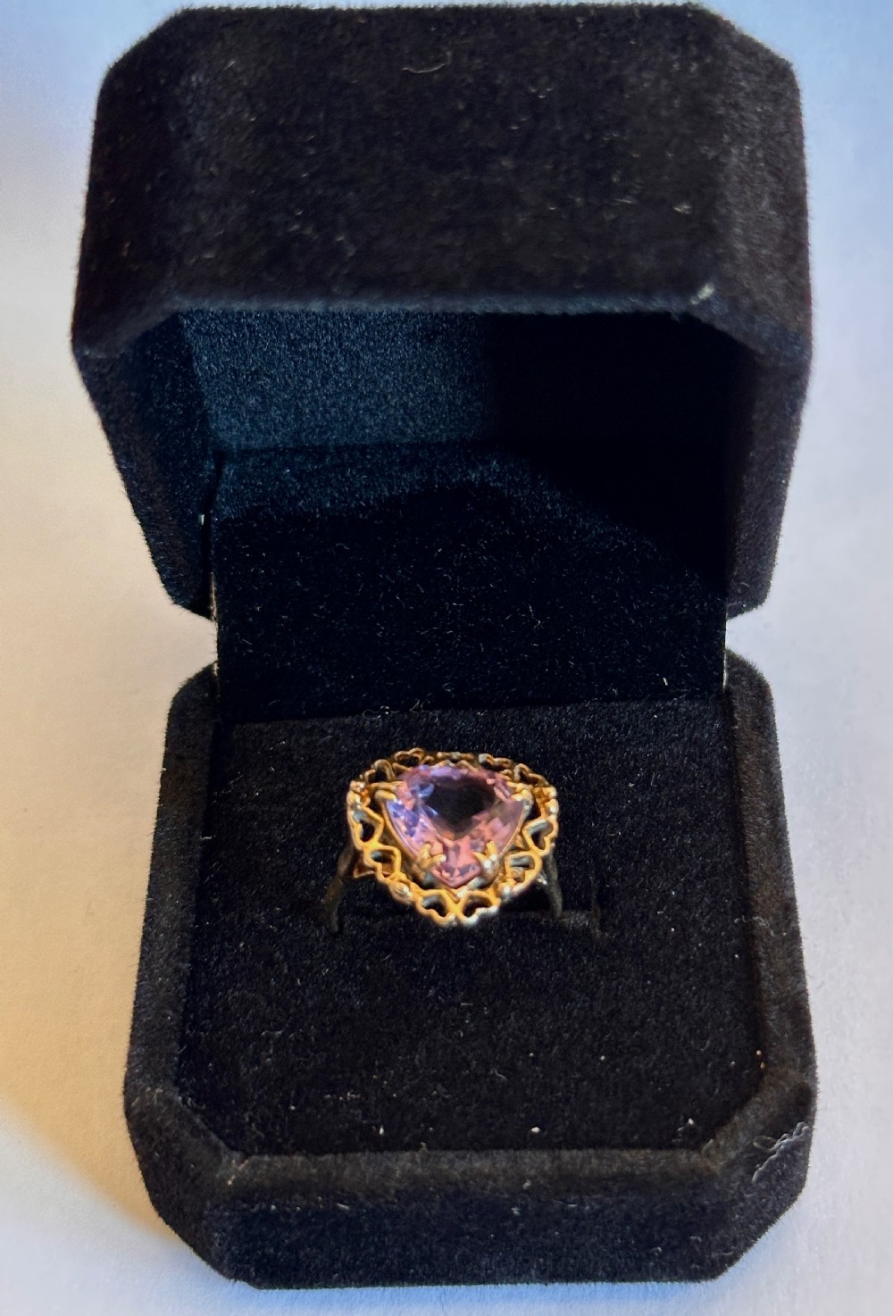 A yellow gold ring featuring a heart-cut purple amethyst set within an openwork heart-motif border and a hallmarked band. View VI