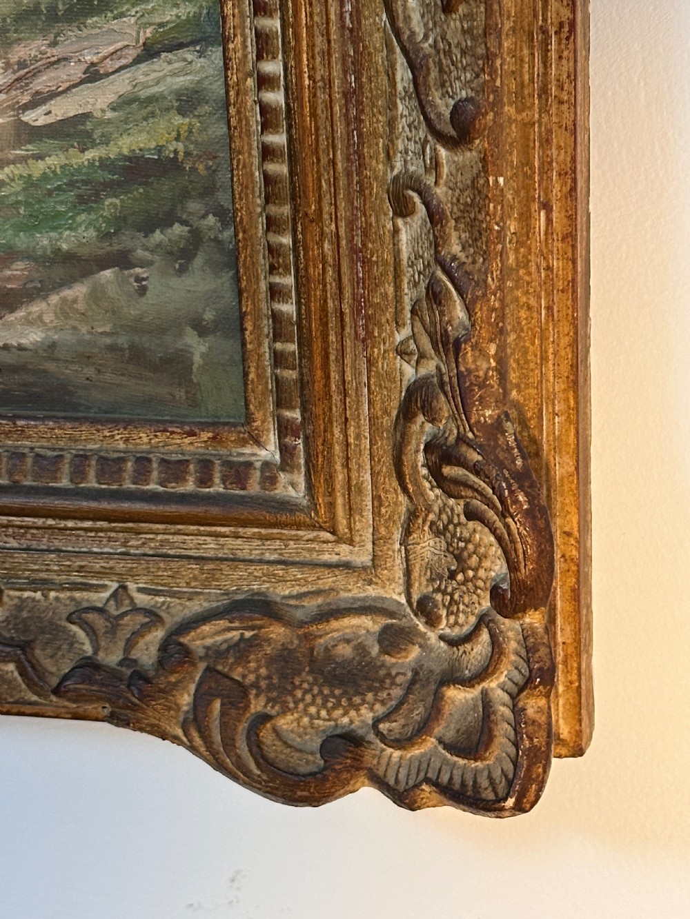 An antique landscape oil painting depicting a calm river flowing through a dense forest, housed in an ornate gilded frame. View III