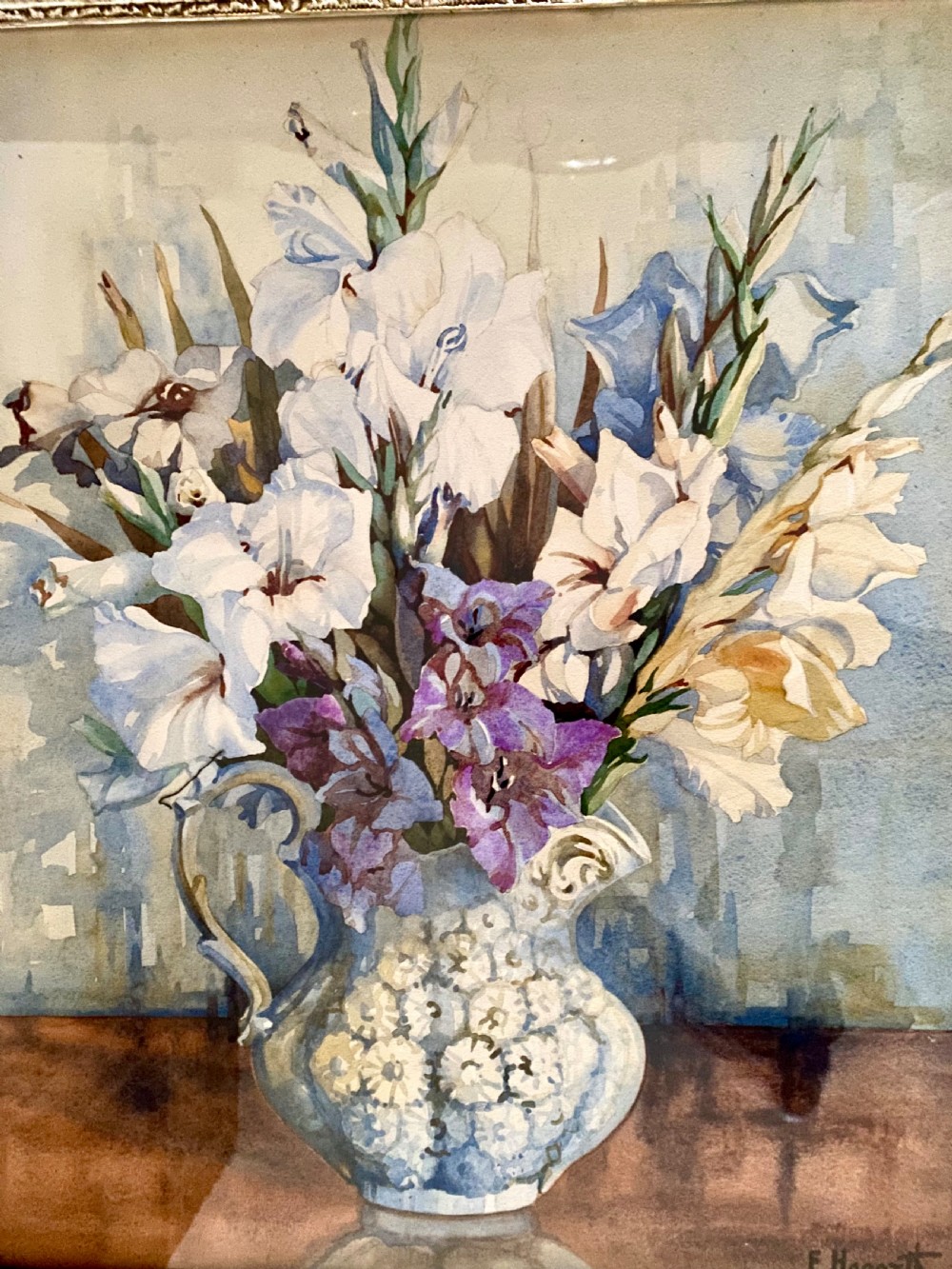A framed watercolour painting depicting white and purple gladioli in an ornate ceramic jug, presented within a carved gilt frame. View III