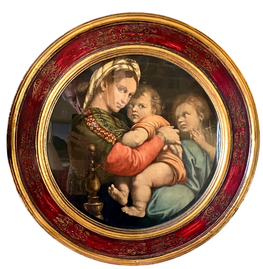 A circular framed fine art print depicting the Virgin Mary embracing the Christ child beside a young John the Baptist, set within a red and gold gilded round frame.