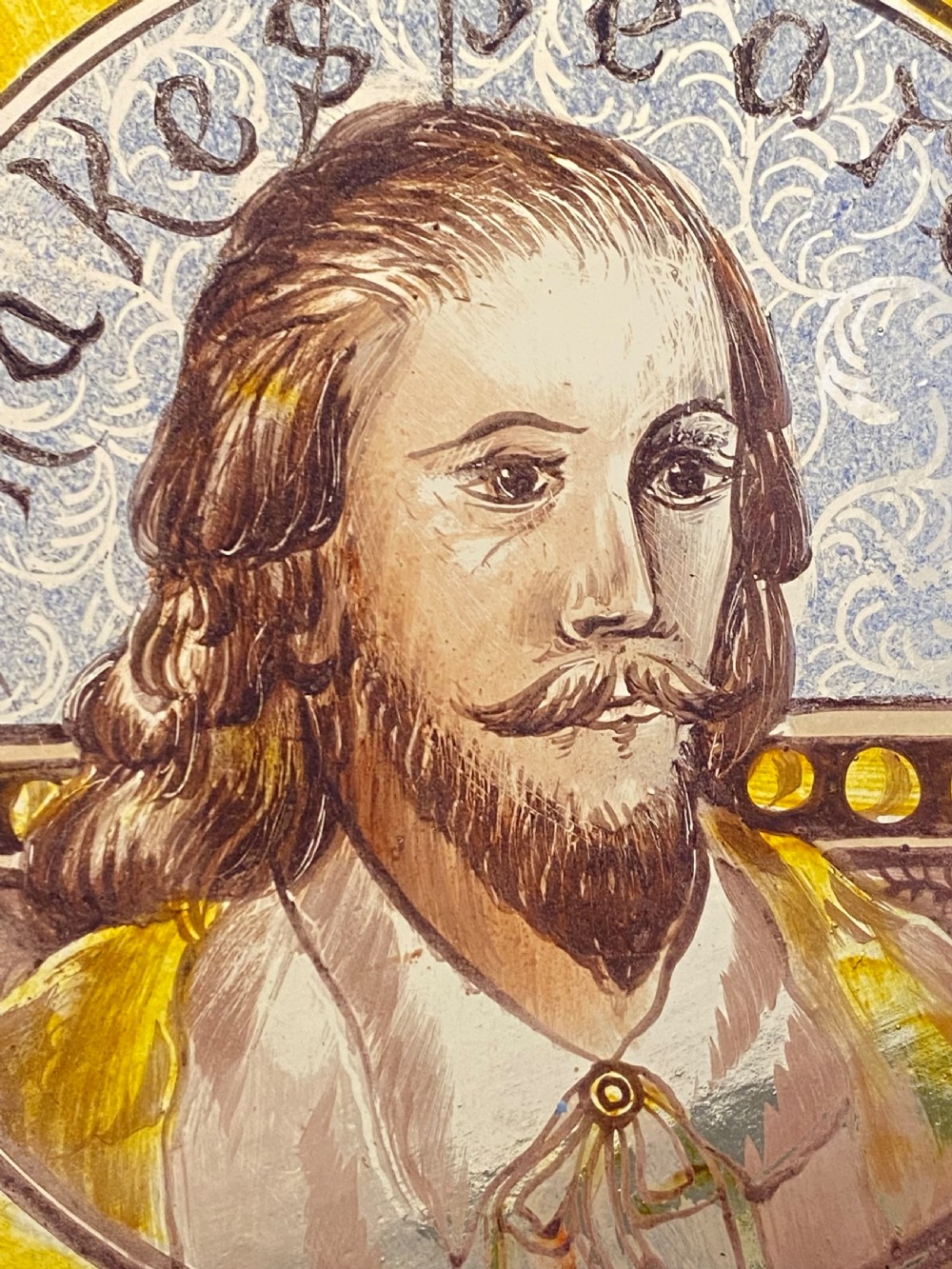 A rectangular framed leaded stained glass panel featuring a central painted roundel portrait of William Shakespeare surrounded by colourful geometric patterns. View III