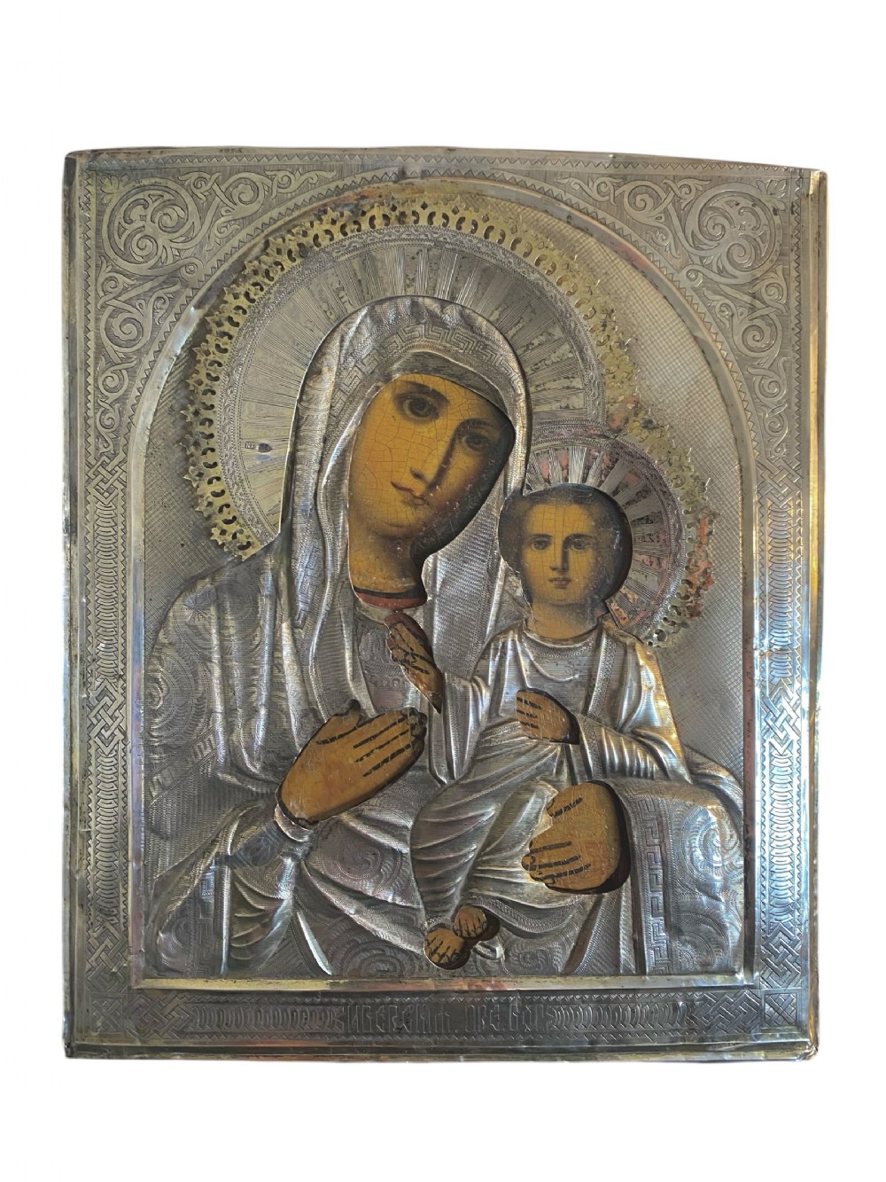 A Russian Orthodox wooden icon encased in an intricately chased silver oklad portraying the Mother of God and Infant Christ.