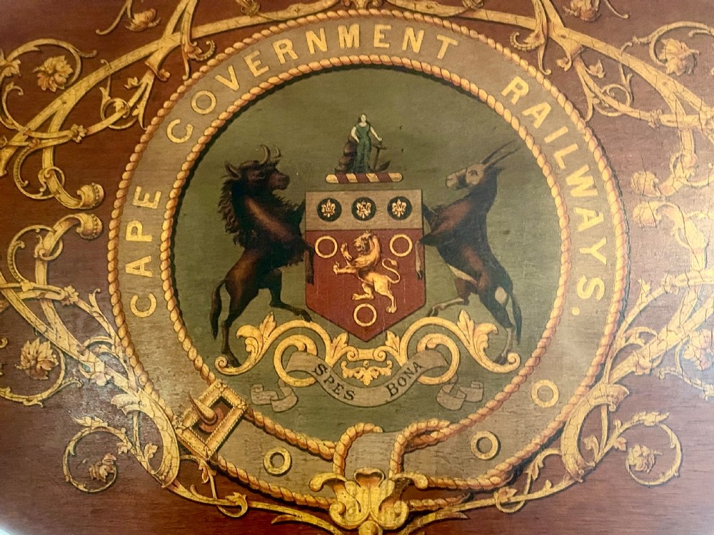 An oval dark wood plaque inscribed with Cape Government Railways featuring a painted coat of arms and gilded floral scrollwork. View III