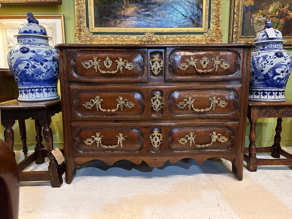 An 18th-century French oak serpentine chest of drawers featuring three rows of moulded drawer fronts and decorative brass handles. View II