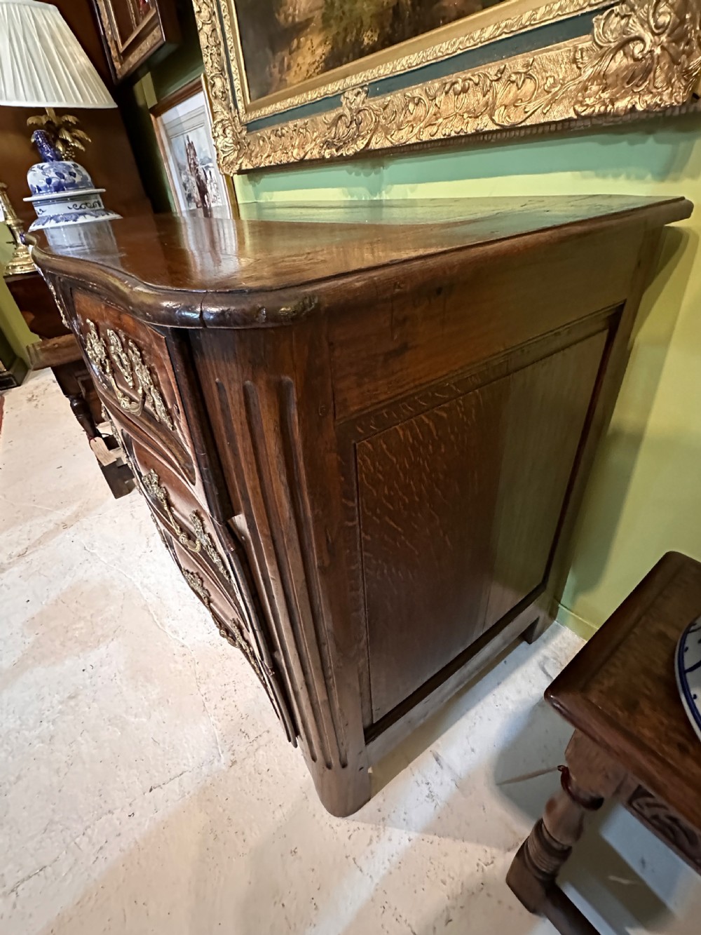 An 18th-century French oak serpentine chest of drawers featuring three rows of moulded drawer fronts and decorative brass handles. View V