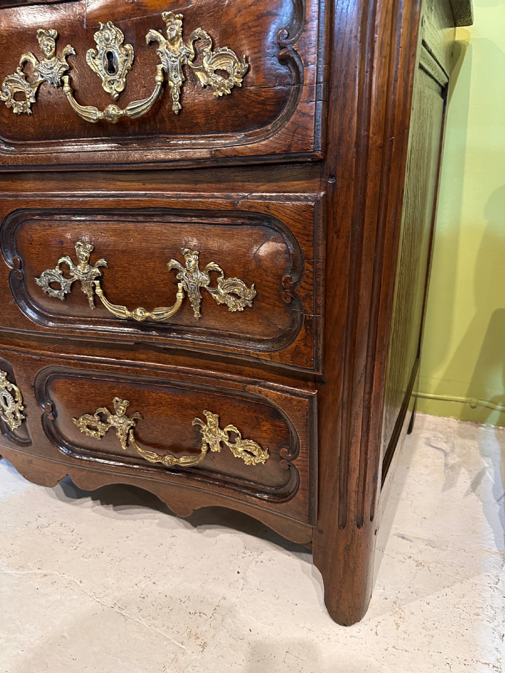 An 18th-century French oak serpentine chest of drawers featuring three rows of moulded drawer fronts and decorative brass handles. View VIII
