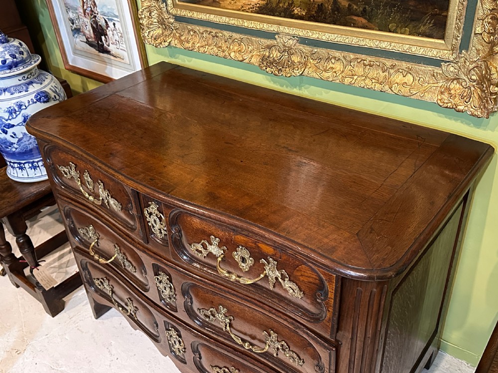 An 18th-century French oak serpentine chest of drawers featuring three rows of moulded drawer fronts and decorative brass handles. View XI