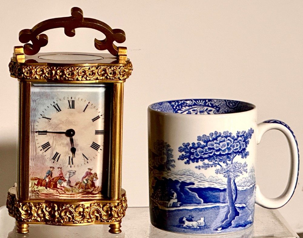 A French gilded brass carriage clock featuring an ornate top handle, detailed relief scrollwork borders, and a porcelain dial decorated with an equestrian scene. View X