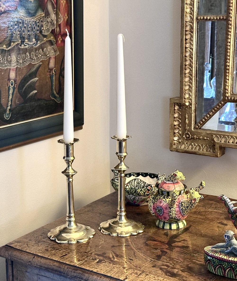 A pair of Georgian brass candlesticks with scalloped bases, turned knopped stems, and matching scalloped drip nozzles. View V