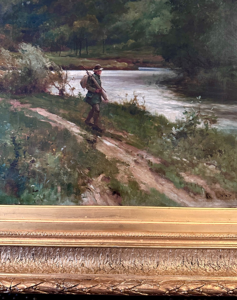 An antique late Victorian oil painting depicting a figure walking along a riverbank path in a rural countryside landscape, framed in a moulded giltwood frame. View III
