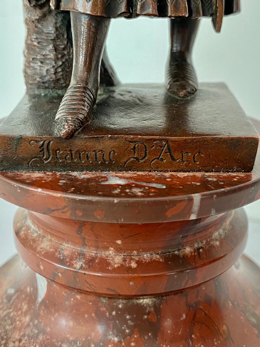 A 19th-century dark bronze sculpture depicting Joan of Arc in suit of armour with a sword, mounted on a round reddish marble base. View X