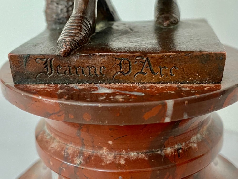 A 19th-century dark bronze sculpture depicting Joan of Arc in suit of armour with a sword, mounted on a round reddish marble base. View XI