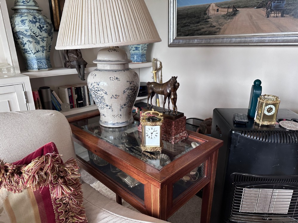 An antique French brass carriage clock featuring serpentine glass panels, scrollwork borders, a white enamel dial with Roman numerals, and a carrying handle. View X