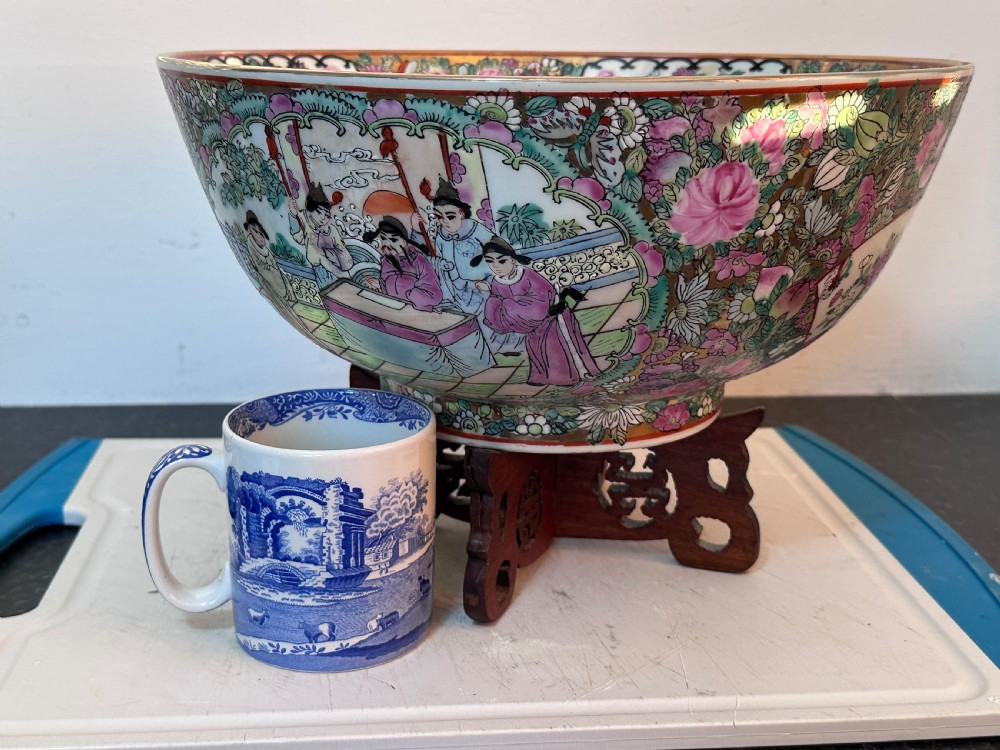 A rounded Chinese Famille Rose porcelain bowl decorated with vibrant pink floral enamelling and figural court scenes, resting on a carved dark wooden stand. View X