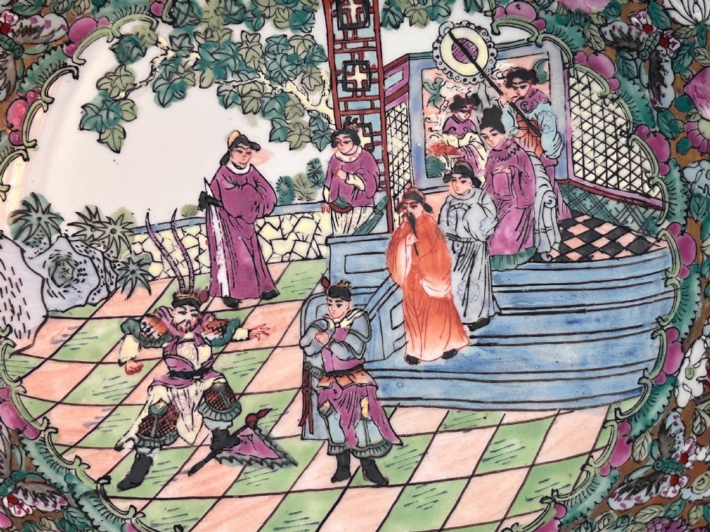 A rounded Chinese Famille Rose porcelain bowl decorated with vibrant pink floral enamelling and figural court scenes, resting on a carved dark wooden stand. View XI