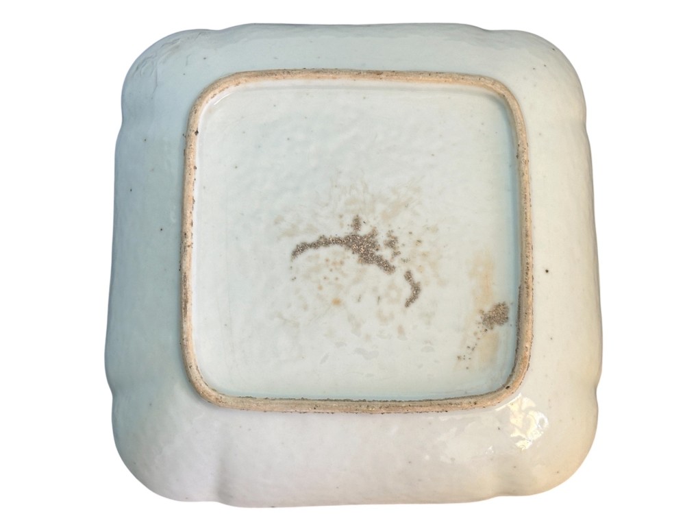 A square Chinese porcelain dish with lobed corners featuring painted reserves of figural court scenes, birds, and flowers set against a dense green scroll and butterfly ground. View V