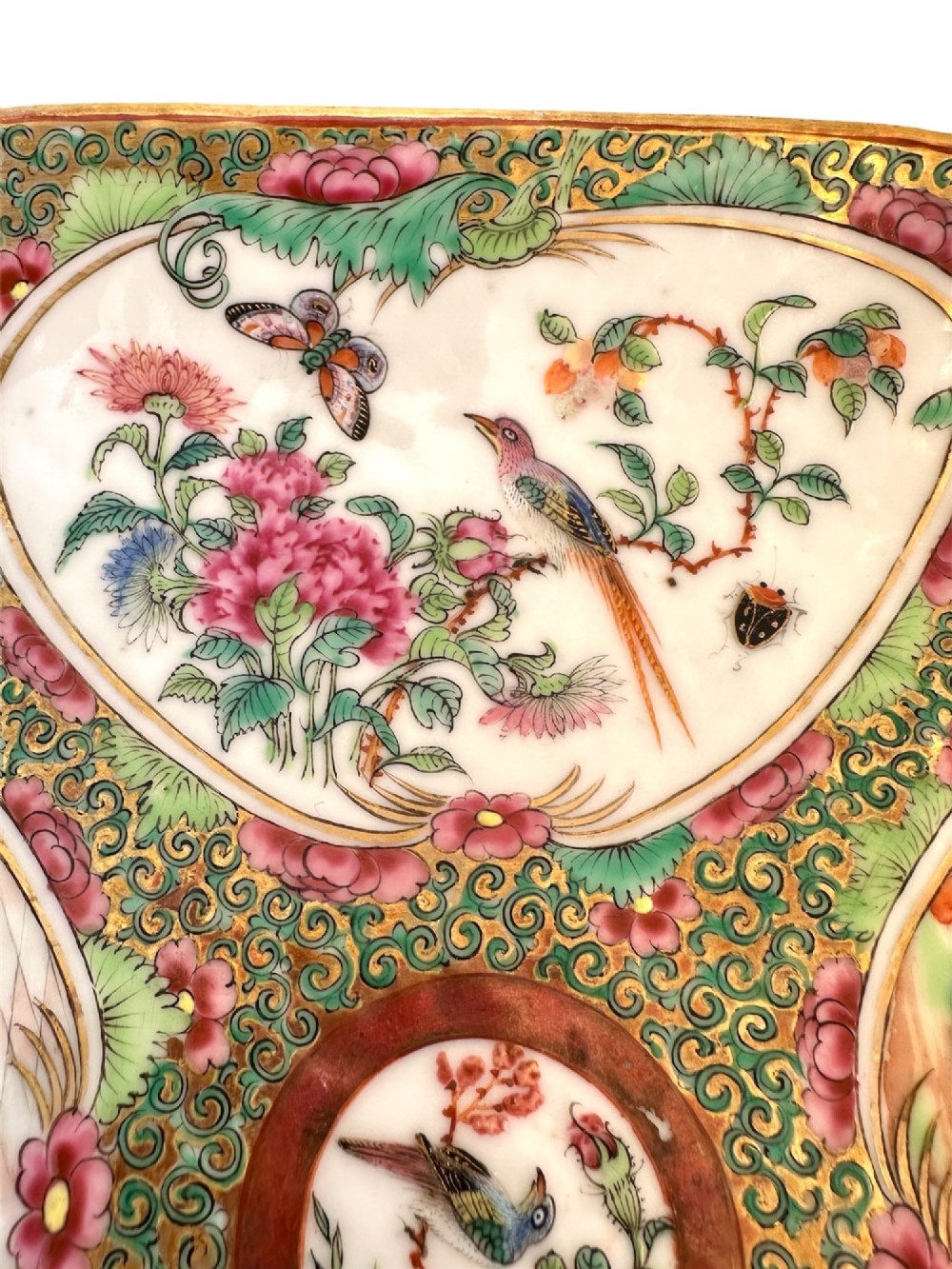 A square Chinese porcelain dish with lobed corners featuring painted reserves of figural court scenes, birds, and flowers set against a dense green scroll and butterfly ground. View VI