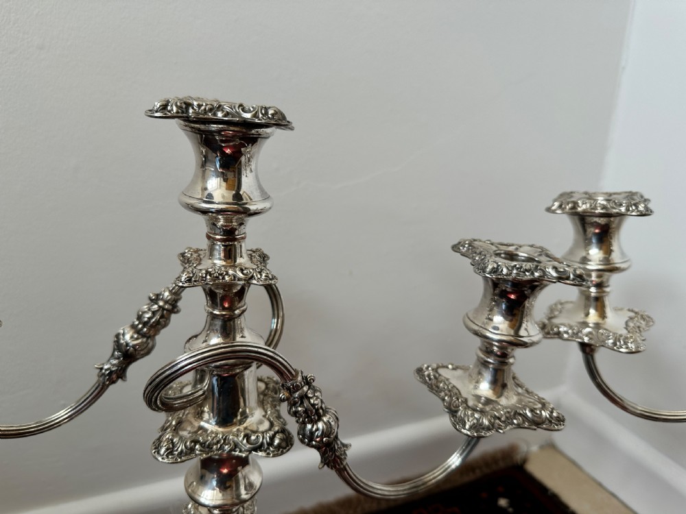 A matching pair of silver-plated three-light candelabra featuring ornate scroll-formed arms, foliate-moulded bases, and white taper candles. View II