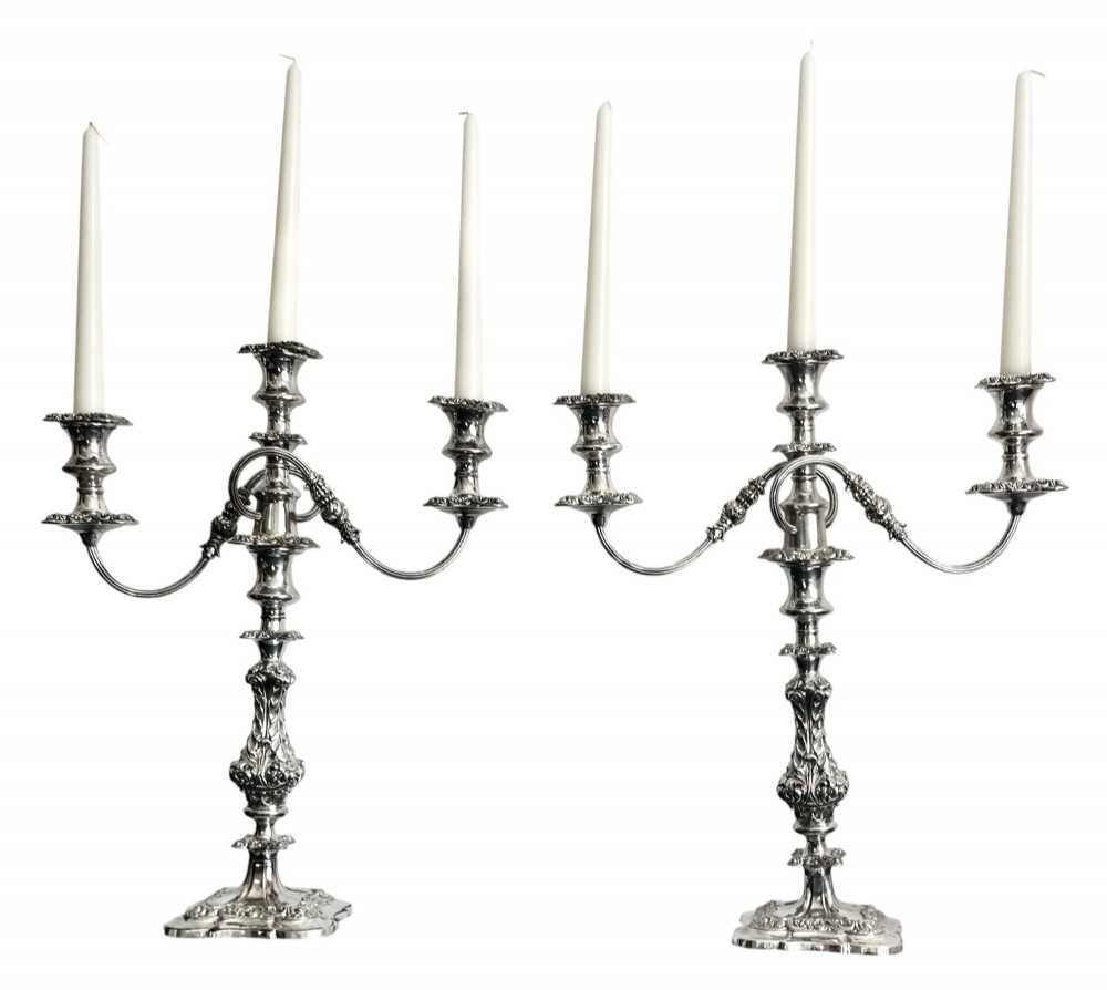 A matching pair of silver-plated three-light candelabra featuring ornate scroll-formed arms, foliate-moulded bases, and white taper candles.