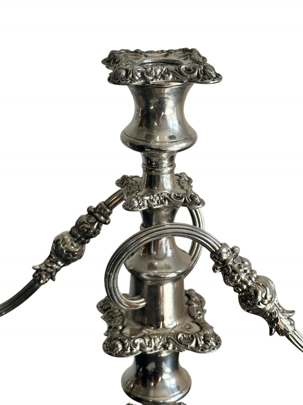 A matching pair of silver-plated three-light candelabra featuring ornate scroll-formed arms, foliate-moulded bases, and white taper candles. View IV