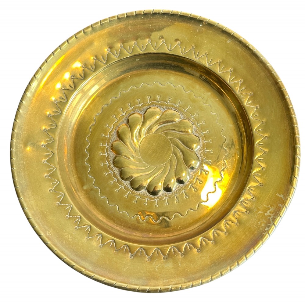 A circular brass alms dish featuring a central gadrooned swirl motif surrounded by punched geometric border patterns. View II