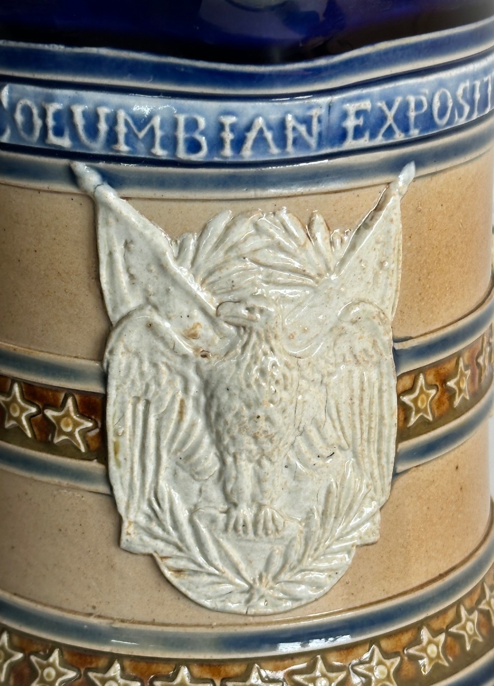 Doulton Lambeth salt-glazed stoneware jug featuring deep cobalt blue borders, buff central body, star motifs, and a relief portrait medallion of Christopher Columbus. View V