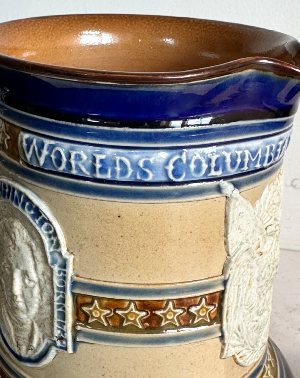 Doulton Lambeth salt-glazed stoneware jug featuring deep cobalt blue borders, buff central body, star motifs, and a relief portrait medallion of Christopher Columbus. View VII
