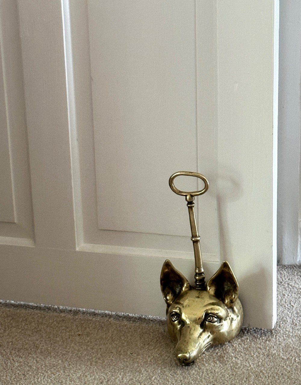 A cast brass doorstop shaped as a fox head with an attached vertical shaft ending in an oval handle. View VI