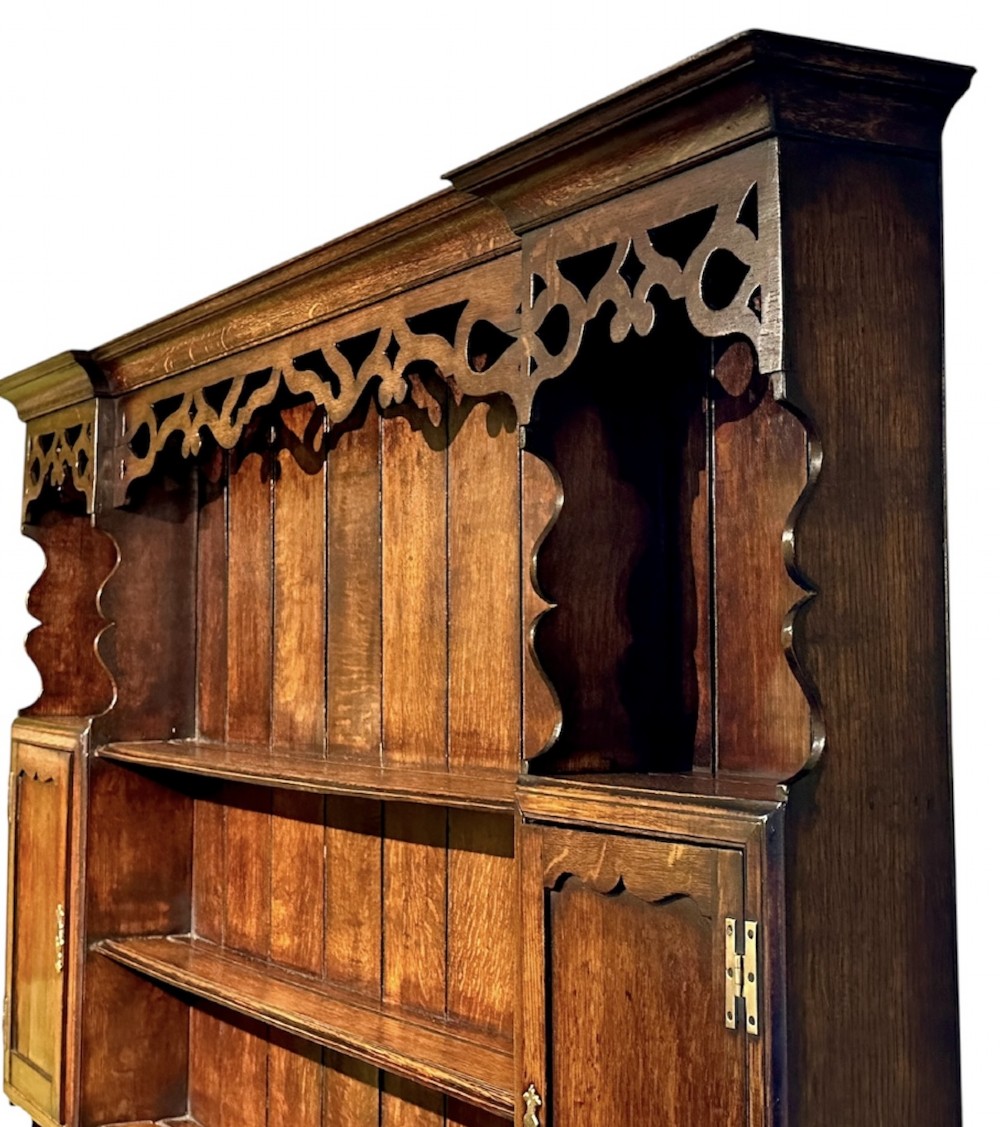 A dark oak George III dresser featuring an open plate rack top with side cupboards above three base drawers supported on cabriole legs. View II
