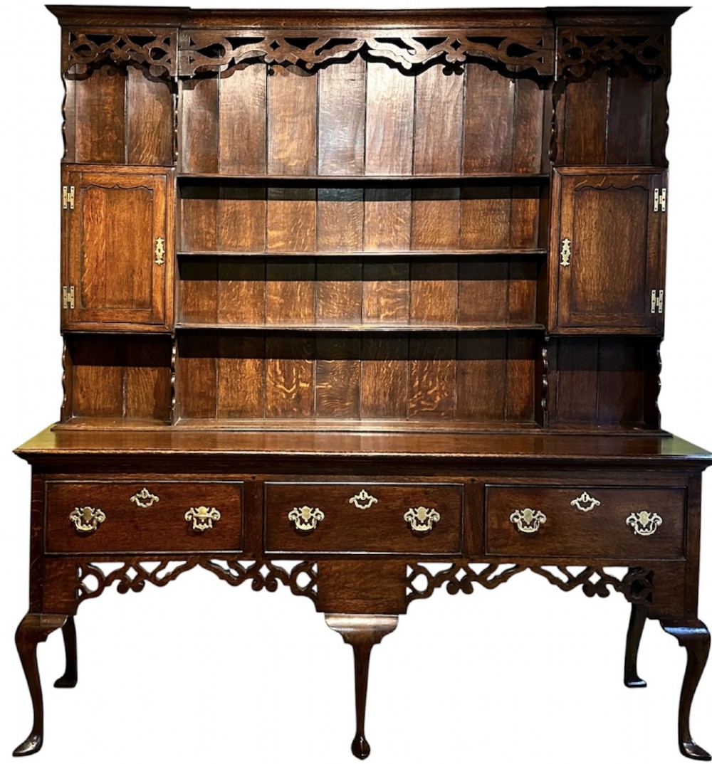 A dark oak George III dresser featuring an open plate rack top with side cupboards above three base drawers supported on cabriole legs.