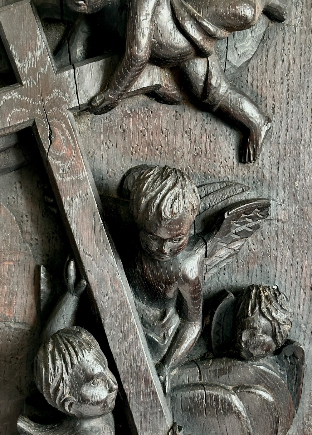 A rectangular dark oak timber panel featuring a high-relief carving of cherubs surrounding a large wooden cross. View VI