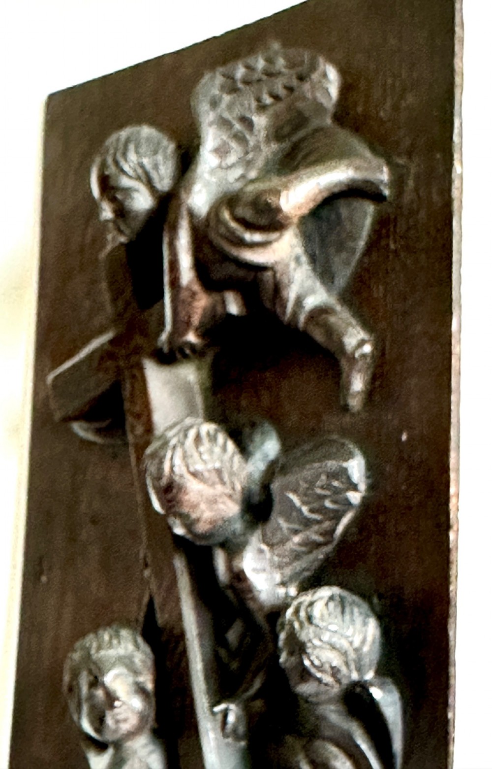 A rectangular dark oak timber panel featuring a high-relief carving of cherubs surrounding a large wooden cross. View VII