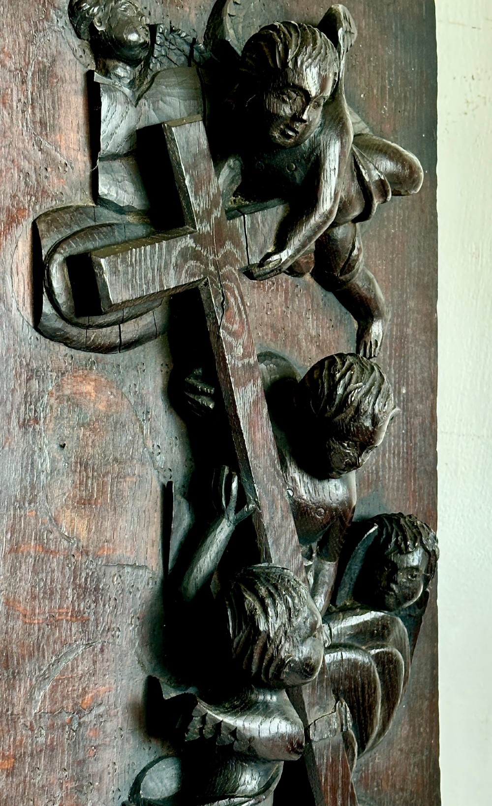 A rectangular dark oak timber panel featuring a high-relief carving of cherubs surrounding a large wooden cross. View IX