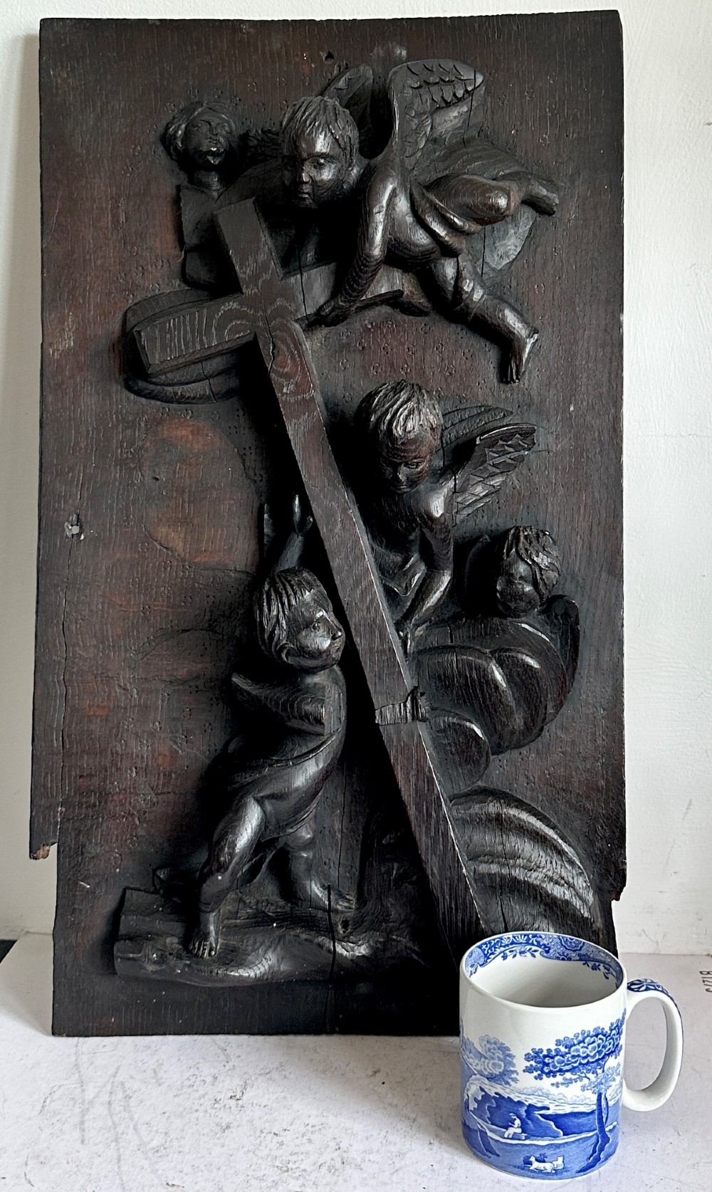 A rectangular dark oak timber panel featuring a high-relief carving of cherubs surrounding a large wooden cross. View II