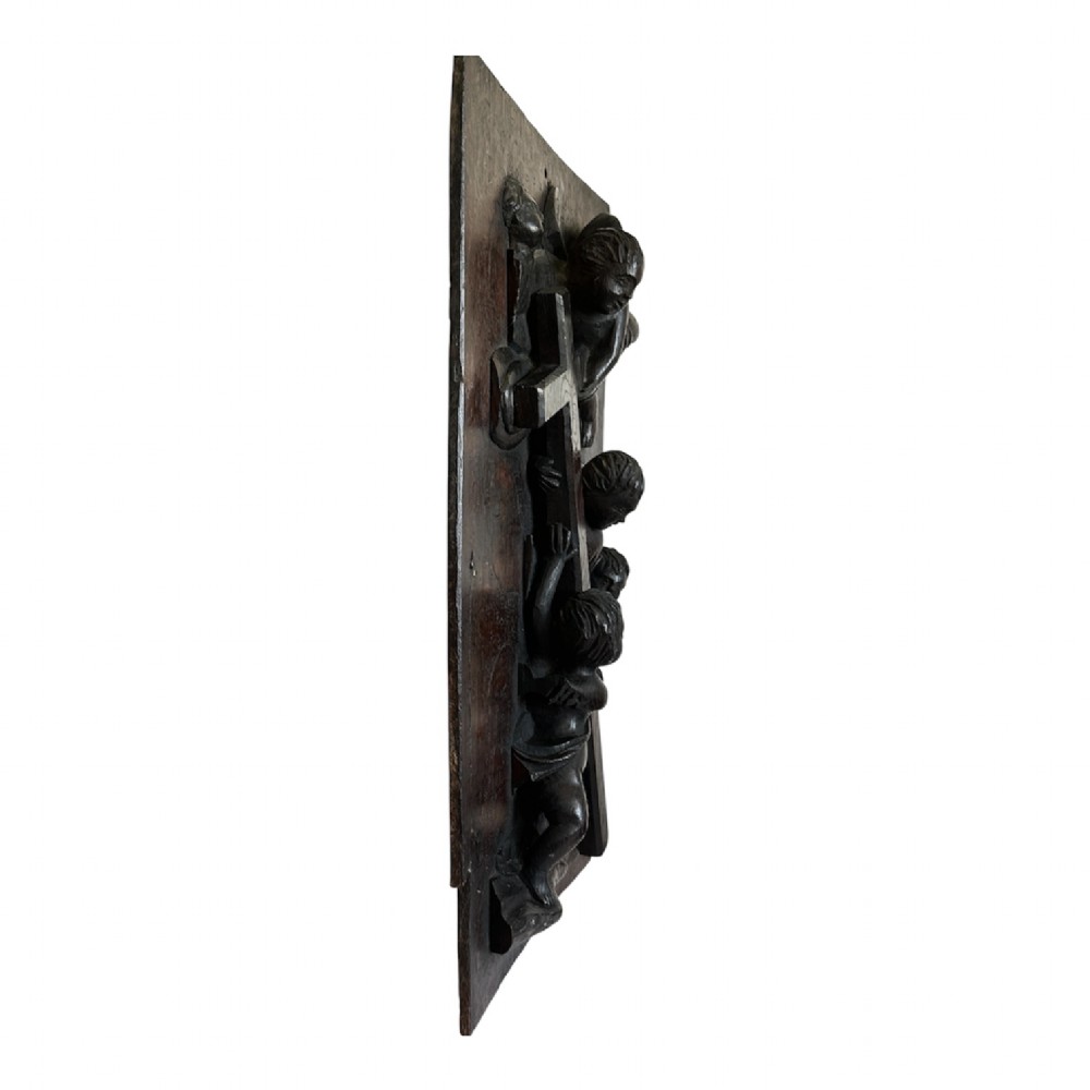 A rectangular dark oak timber panel featuring a high-relief carving of cherubs surrounding a large wooden cross. View XII