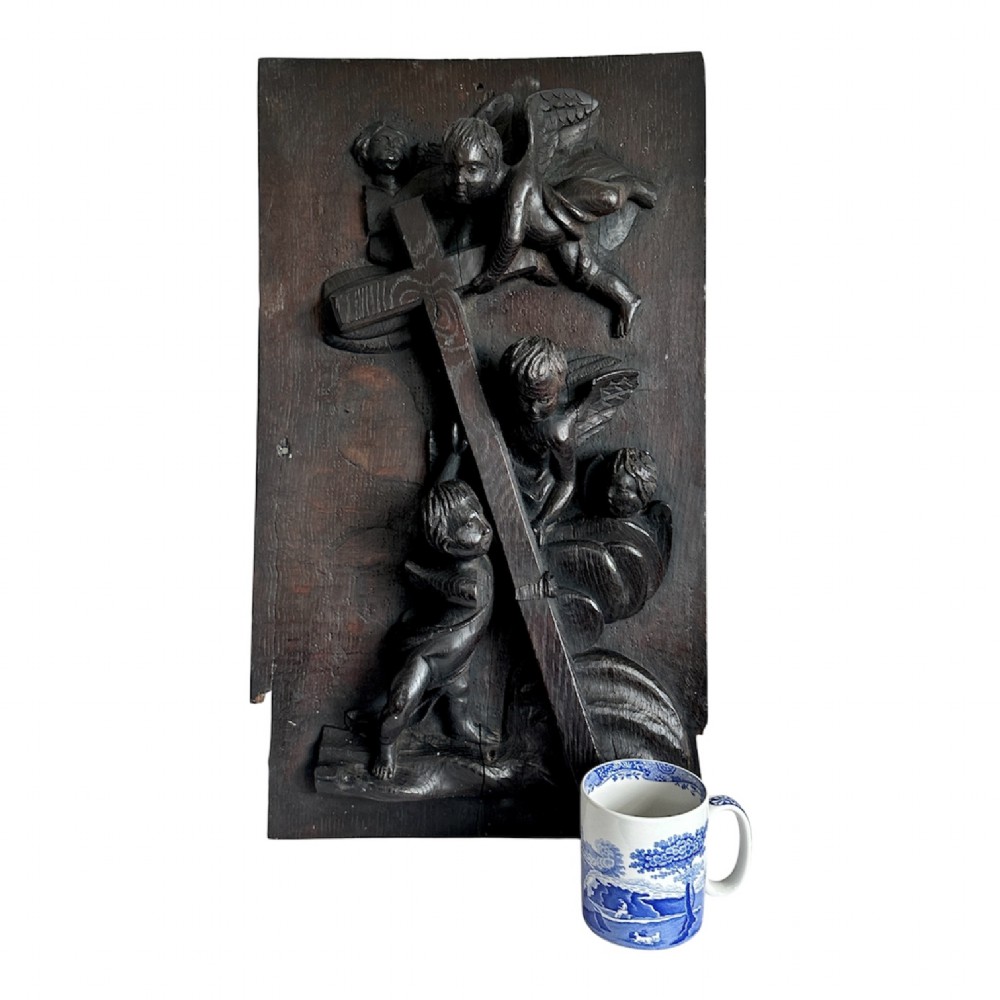 A rectangular dark oak timber panel featuring a high-relief carving of cherubs surrounding a large wooden cross. View XIII